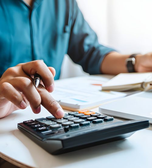 Doing finance, budgeting and tax calculation. Close up woman hand using calculator to calculate home finance, accounting with laptop computer on table, budget management, monthly expenses.