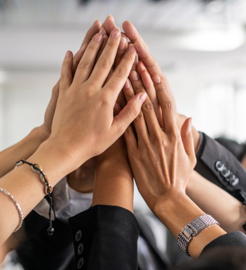 Many happy business people raise hands together with joy and success. Company employee celebrate after finishing successful work project. Corporate partnership and achievement concept.